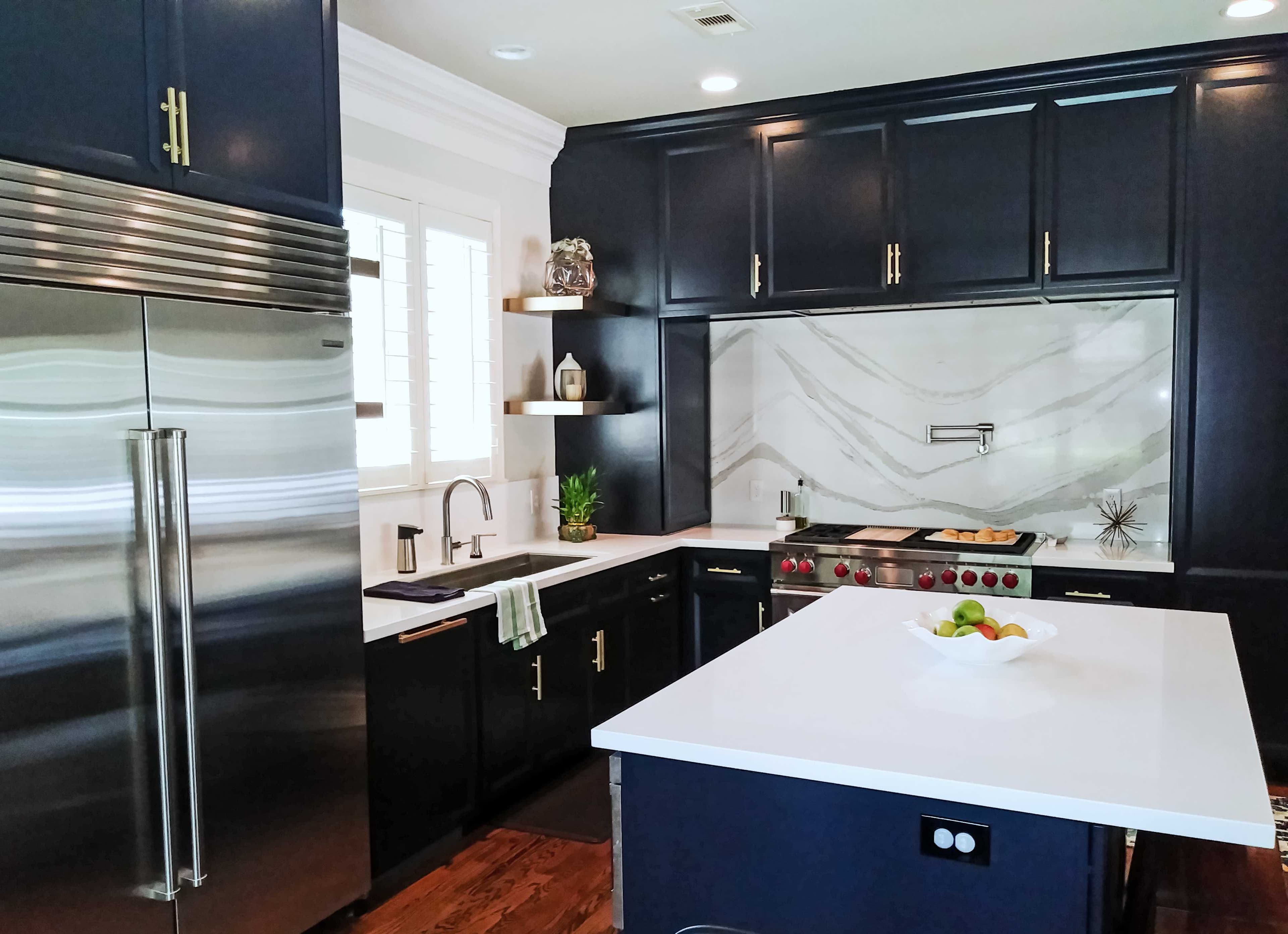 Modern kitchen with navy blue cabinets, gold hardware, white marble backsplash, and a white island.