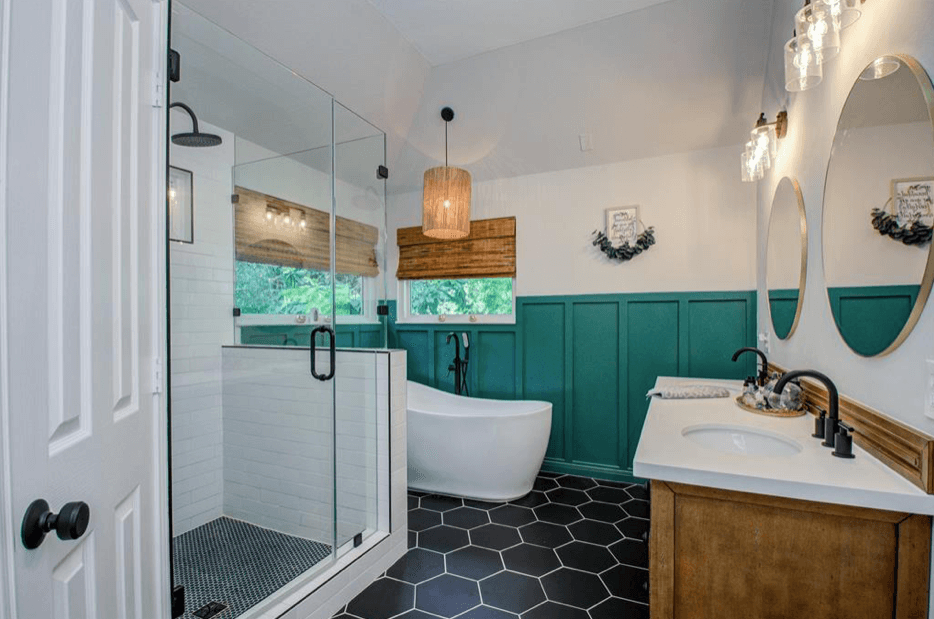 Modern bathroom with teal wainscoting, black hexagonal tiles, glass shower, and a white freestanding tub.