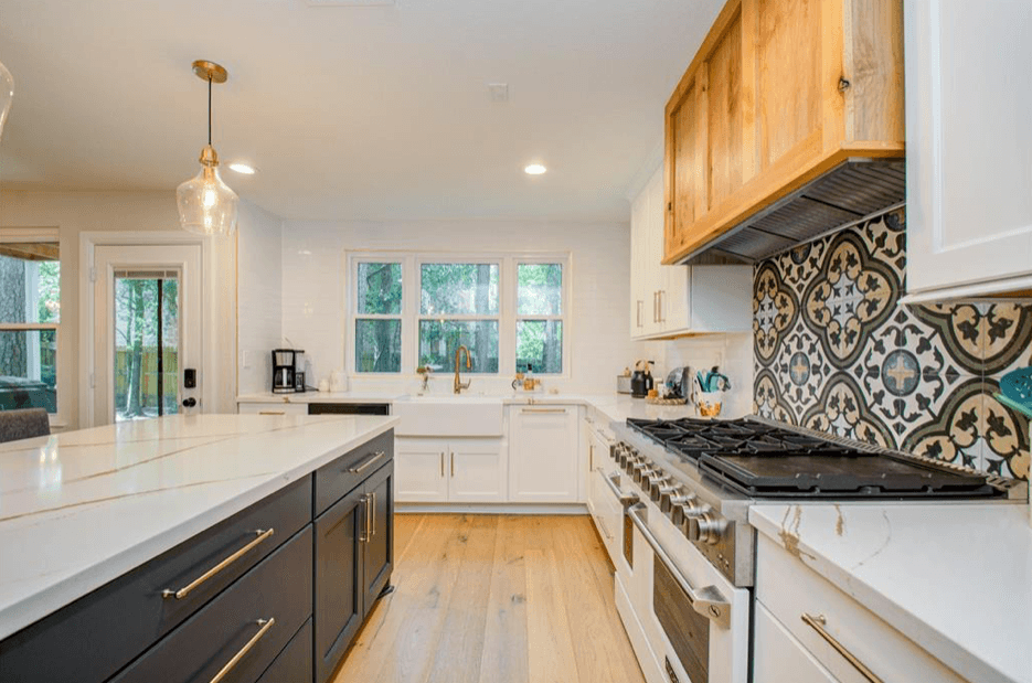 Modern kitchen with white cabinets, dark island, marble countertops, and a patterned tile backsplash.