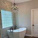 Modern bathroom featuring a white freestanding bathtub, crystal chandelier, and glass-walled shower area.