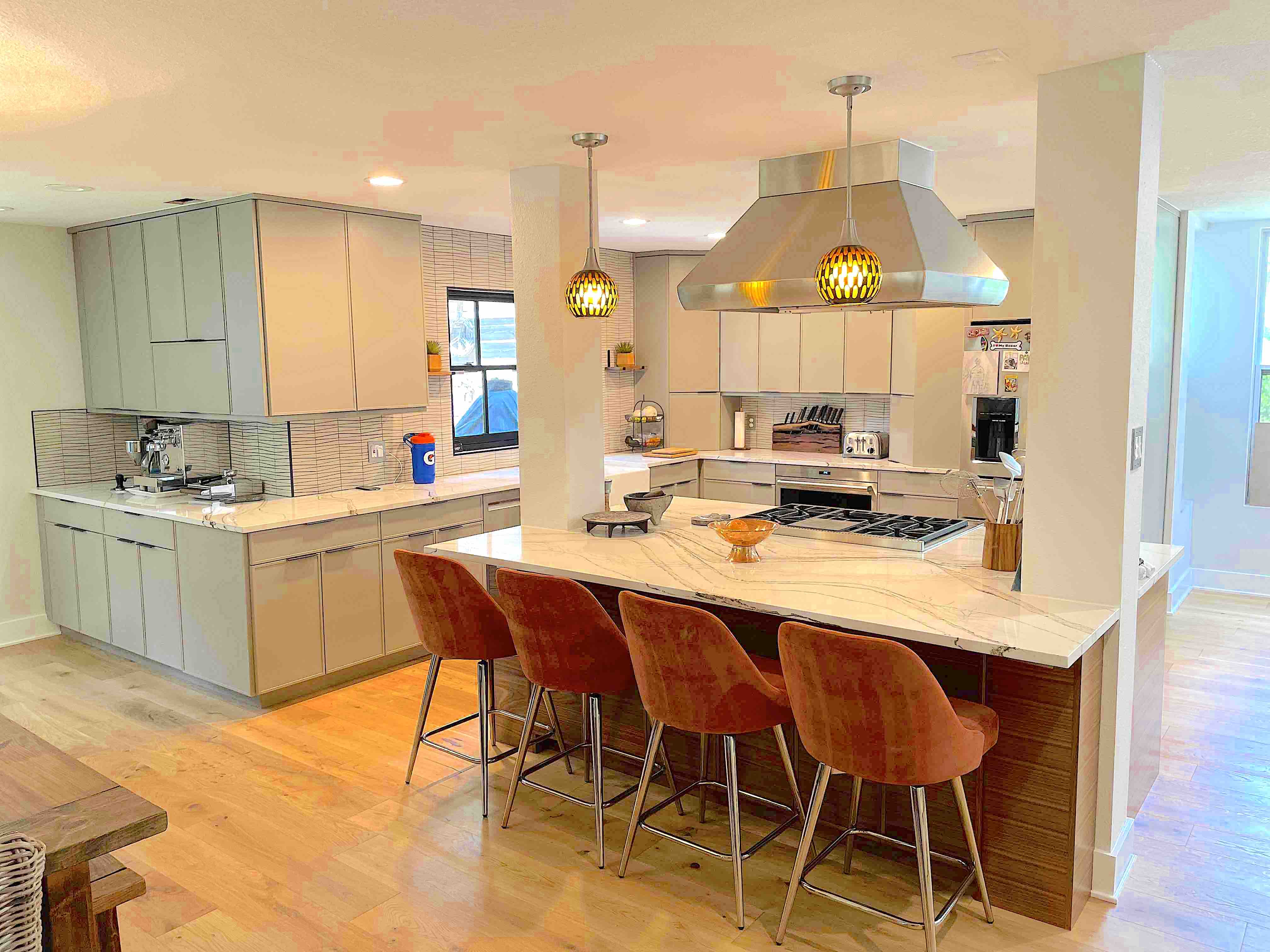 Modern kitchen featuring a marble island, orange velvet bar stools, and light grey cabinetry.