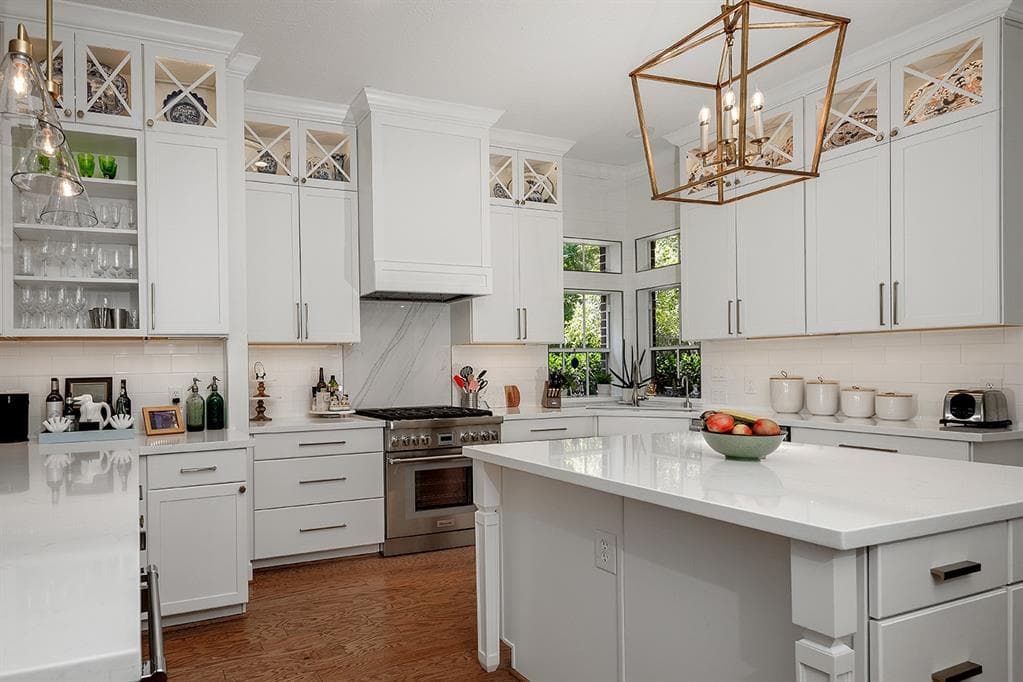 Modern white kitchen with shaker cabinets, marble backsplash, large island, and gold geometric chandelier.